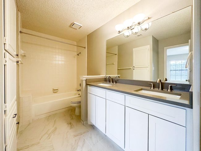 Full bath featuring toilet, shower / bathtub combination, double vanity, marble finish flooring, and a textured ceiling | Image 8