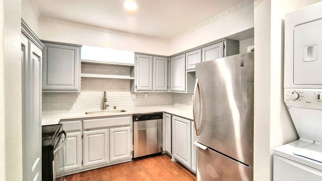 Kitchen with gray cabinets, stacked washer / dryer, tasteful backsplash, sink, and stainless steel appliances | Image 15