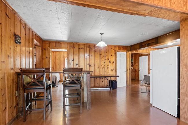 Kitchen with white fridge, wooden walls, hanging light fixtures, and a breakfast bar area | Image 11