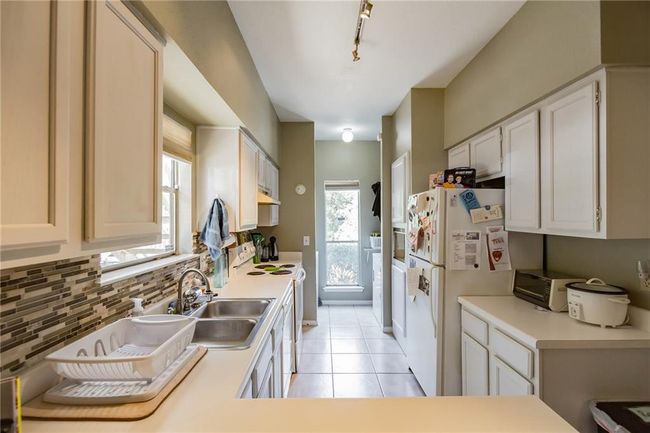 Kitchen featuring a sink, white appliances, decorative backsplash, light tile patterned flooring, and under cabinet range hood | Image 9