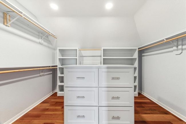 Spacious walk-in closet with ample shelving and hanging space, featuring a central storage island. Bright lighting and wooden flooring enhance the modern appeal. | Image 29
