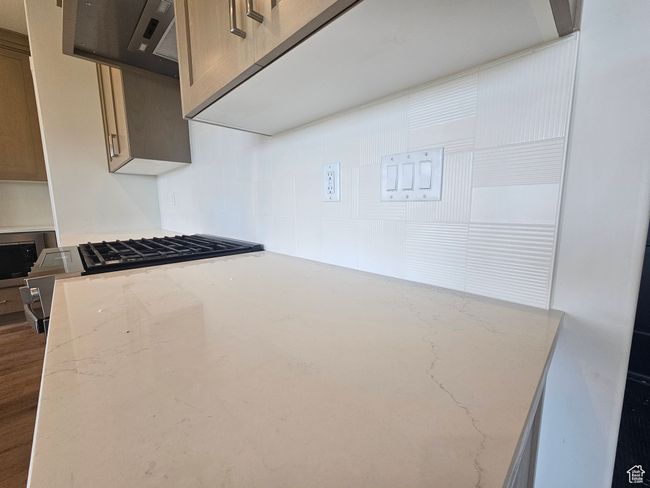 Kitchen view of light stone countertops, stainless steel microwave, stovetop, exhaust hood, and tasteful backsplash | Image 5