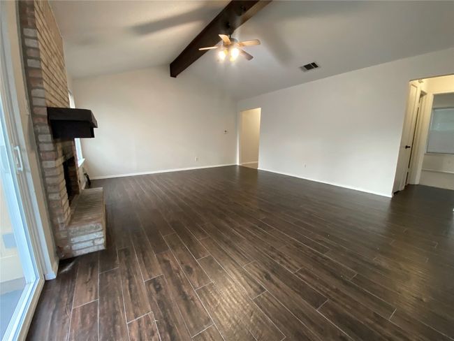 Unfurnished living room with lofted ceiling with beams, dark finished floors, a ceiling fan, a brick fireplace. | Image 6