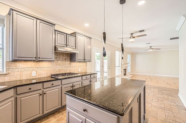 Kitchen featuring ornamental molding, gray cabinetry, under cabinet range hood, stainless steel gas cooktop, and stone tile floors | Image 17