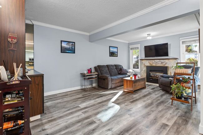 Living room featuring wood finished floors, a stone fireplace, baseboards and crown molding | Image 8