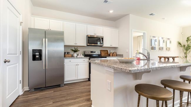 Kitchen featuring a breakfast bar, a sink, dark wood finished floors, stainless steel appliances, and white cabinetry | Image 4