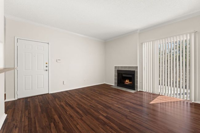 Unfurnished living room featuring a tiled fireplace, dark wood-type flooring, baseboards, and ornamental molding | Image 4