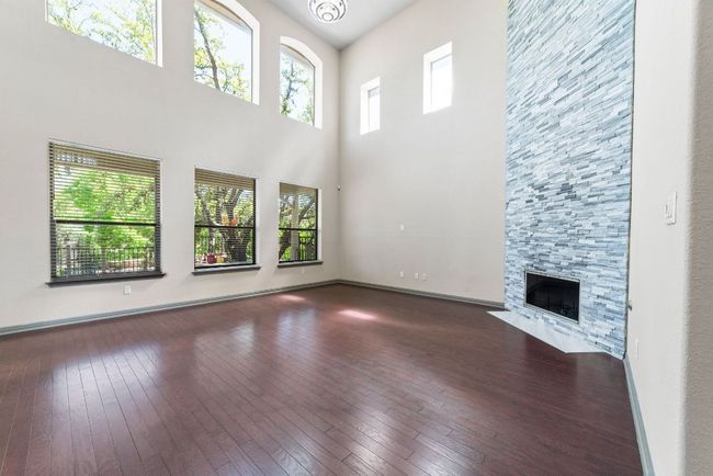 Unfurnished living room featuring wood-type flooring, a towering ceiling, and a fireplace | Image 10