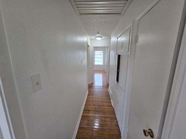 Hall with a textured ceiling, dark wood-style floors, and a textured wall | Image 4