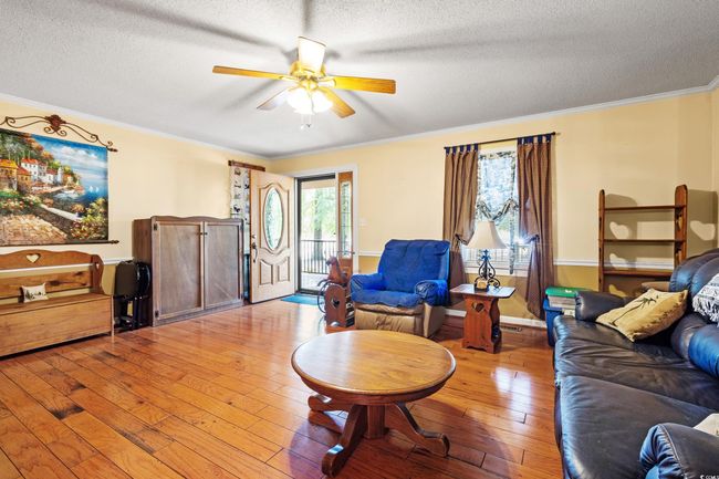 Living room with ceiling fan, a textured ceiling, light wood-style flooring, crown molding, and baseboards | Image 7
