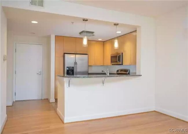 Kitchen featuring light wood-type flooring, a peninsula, visible vents, dark countertops, and stainless steel appliances | Image 8