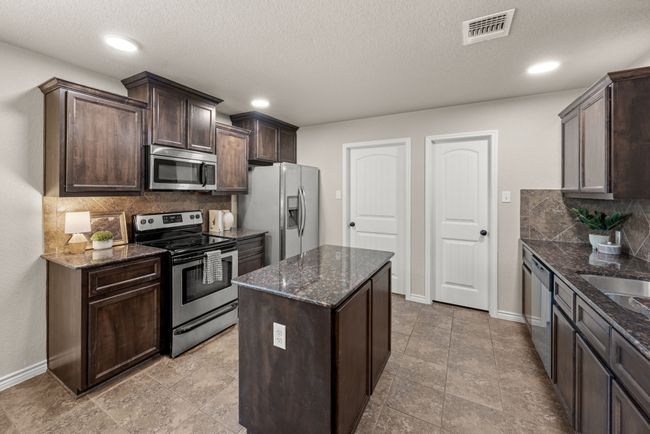 Kitchen featuring stainless steel appliances, dark brown cabinets, dark stone countertops, tasteful backsplash, and a textured ceiling | Image 10