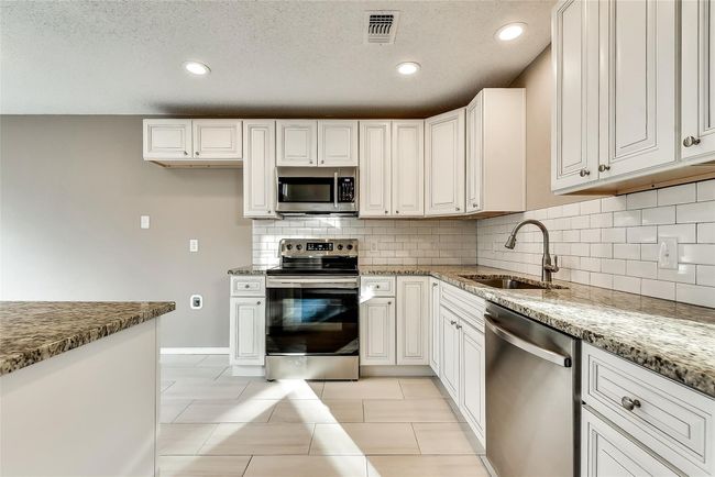 Kitchen featuring stainless steel appliances, backsplash, light stone counters, recessed lighting, and white cabinets | Image 6