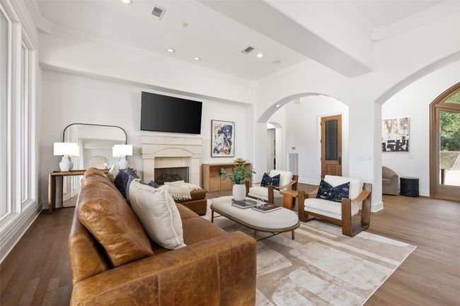 Living area with arched walkways, a fireplace, crown molding, wood finished floors, and recessed lighting | Image 5
