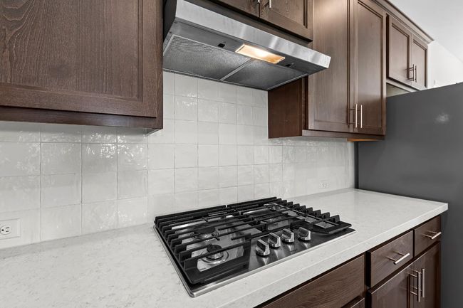 Kitchen with ventilation hood, appliances with stainless steel finishes, backsplash, dark brown cabinetry, and light stone countertops | Image 39