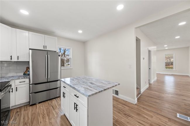 Kitchen with white cabinets, decorative backsplash, a wealth of natural light, a kitchen island, and stainless steel refrigerator | Image 10