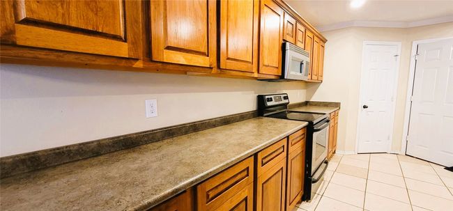 Kitchen with brown cabinetry, light tile patterned floors, baseboards, stainless steel appliances, and ornamental molding | Image 5