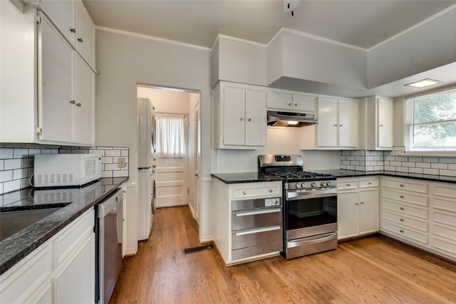 Kitchen with appliances with stainless steel finishes, under cabinet range hood, light wood-style floors, white cabinetry, and tasteful backsplash | Image 15