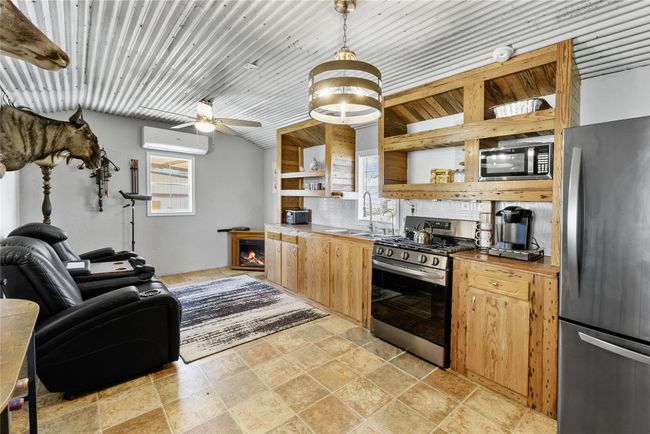 Kitchen featuring a wall mounted AC, stone tile flooring, open shelves, stainless steel appliances, and a sink | Image 8