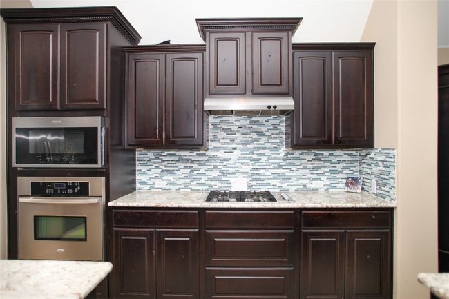 Kitchen featuring stainless steel appliances, dark brown cabinetry, under cabinet range hood, and decorative backsplash | Image 12