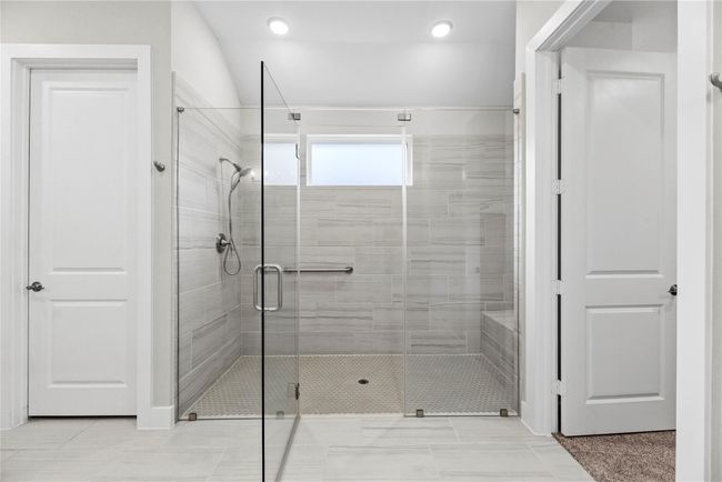 The spa-inspired walk-in shower is a true showstopper, showcasing a frameless glass enclosure, built-in bench seating, and sleek tile surround delivering the perfect blend of luxury, comfort, and accessibility in the owner’s ensuite. | Image 31