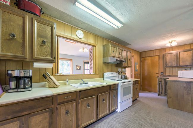 Kitchen featuring electric stove, under cabinet range hood, light countertops, wood walls, and light colored carpet | Image 15