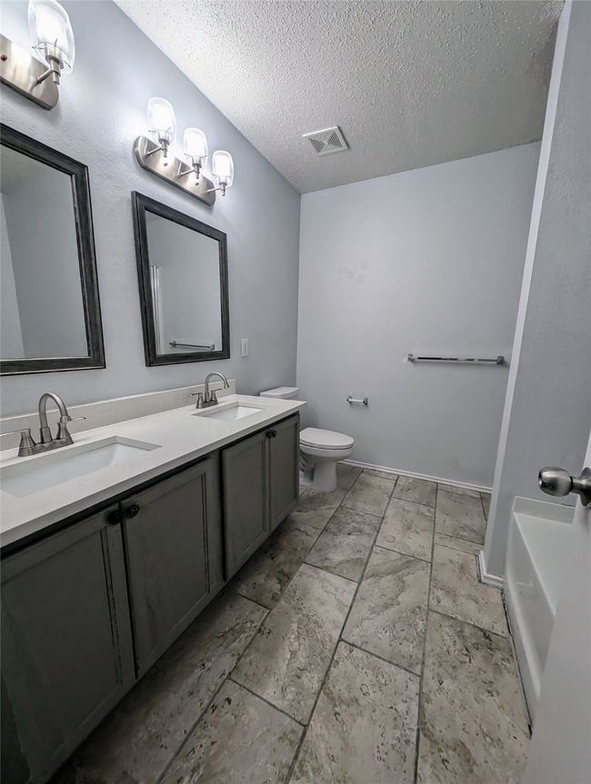 Bathroom with double vanity, a textured ceiling, toilet, and a tub | Image 9
