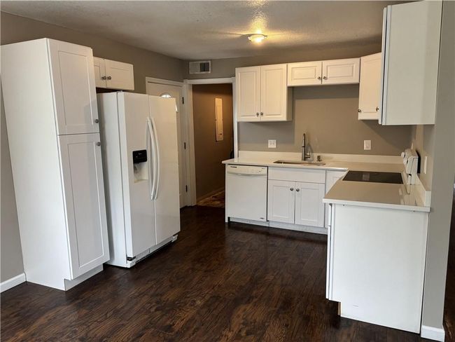 Kitchen featuring white appliances, white cabinets, a sink, visible vents, and dark wood-type flooring | Image 8