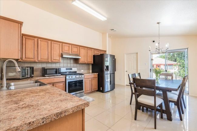 Kitchen with stainless steel appliances, under cabinet range hood, a chandelier at dinning area, a sink, and decorative backsplash | Image 6