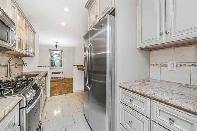 Kitchen featuring stainless steel dishwasher, radiator, backsplash, light stone countertops, and glass insert cabinets | Image 20