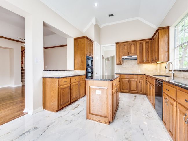Kitchen with under cabinet range hood, black appliances, granite counters, a kitchen island, and crown molding. | Image 14