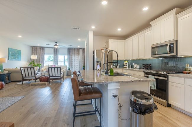 Kitchen with stainless steel appliances, open floor plan, light stone countertops, decorative backsplash, and white cabinetry | Image 10