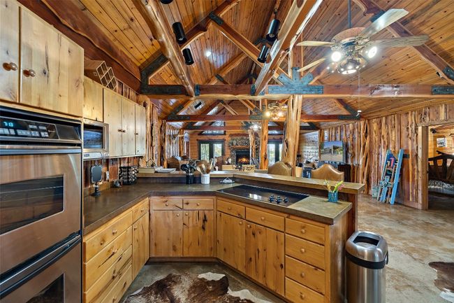 Kitchen featuring wood ceiling, a peninsula, wood walls, black electric cooktop, and dark countertops | Image 22