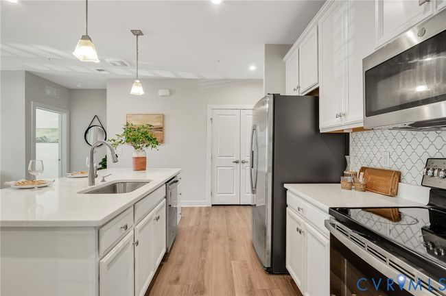 Kitchen with stainless steel appliances, white cabinetry, an island with sink, light wood-type flooring, and recessed lighting | Image 8