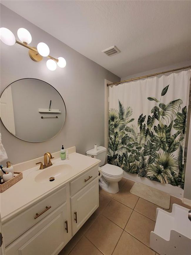 This bathroom features a modern design with a round mirror, stylish light fixtures, and a vanity with a light countertop and gold fixtures. | Image 27