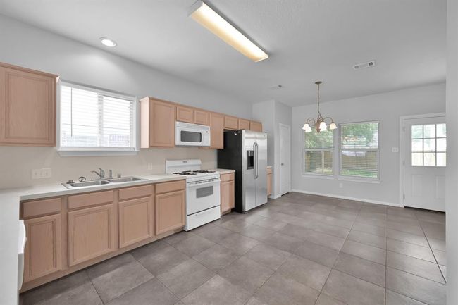 The spacious kitchen and dining area features an open layout. This kitchen boasts abundant cabinetry in a natural wood finish, and a double sink under a window for plenty of natural light. | Image 10