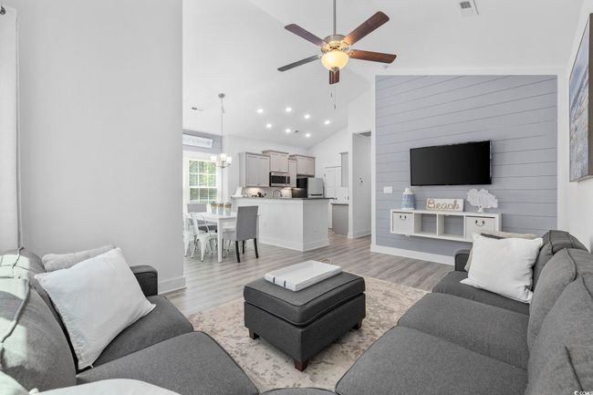 Living room featuring ceiling fan with notable chandelier, baseboards, high vaulted ceiling, and light wood-type flooring | Image 5