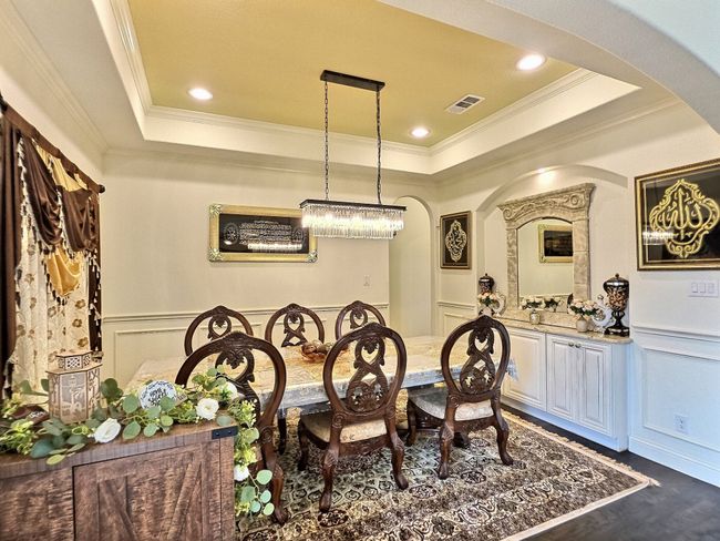 Dining space featuring arched walkways, a raised ceiling, a decorative wall, crown molding, and dark wood-style flooring | Image 8