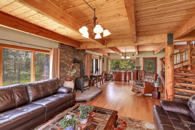 Living room with a chandelier, a wood stove, a wood ceiling with exposed beams, wood-type flooring, and stairway | Image 10