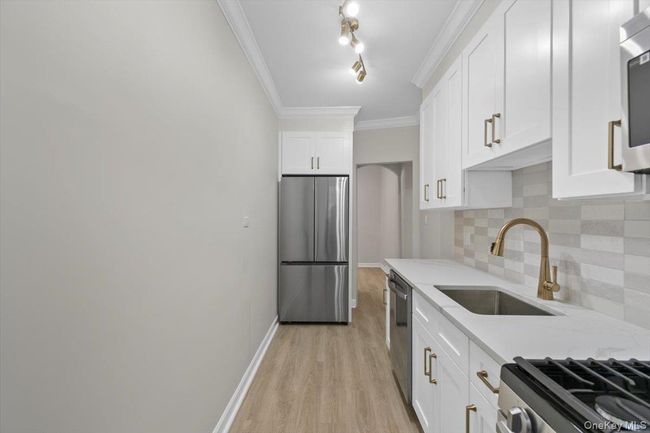 Kitchen with crown molding, stainless steel appliances, white cabinets, light stone countertops, and backsplash | Image 7