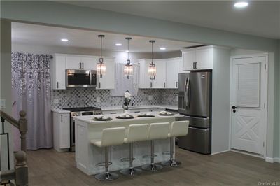 Kitchen with a kitchen island, appliances with stainless steel finishes, hanging light fixtures, dark wood-type flooring, and white cabinets | Image 1