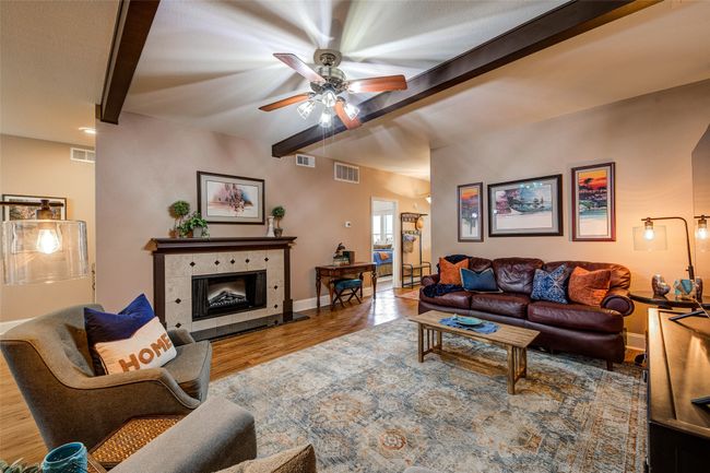 Living area with beam ceiling, a ceiling fan, wood finished floors, and a tiled fireplace | Image 8
