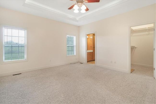 Unfurnished bedroom featuring multiple windows, a walk in closet, a raised ceiling, and light carpet | Image 27