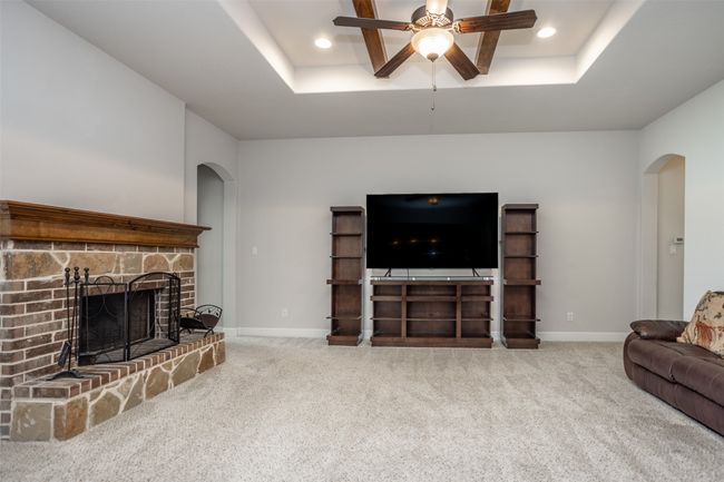 Living room with arched walkways, ceiling fan, a tray ceiling, carpet flooring, and recessed lighting | Image 10
