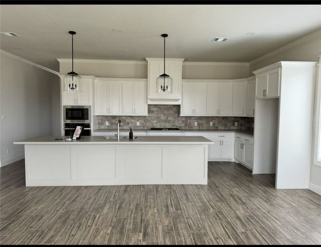 Kitchen featuring stainless steel microwave, cooktop, decorative backsplash, oven, and white cabinets | Image 9