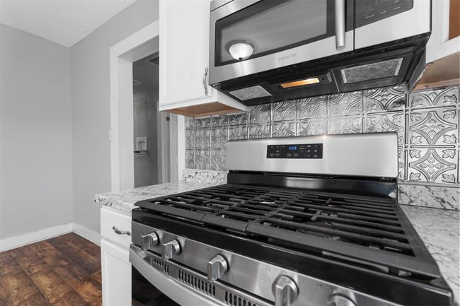 Kitchen with appliances with stainless steel finishes, decorative backsplash, white cabinets, and light stone countertops | Image 6