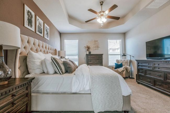 Bedroom with light colored carpet, a tray ceiling, visible vents, and ceiling fan | Image 25