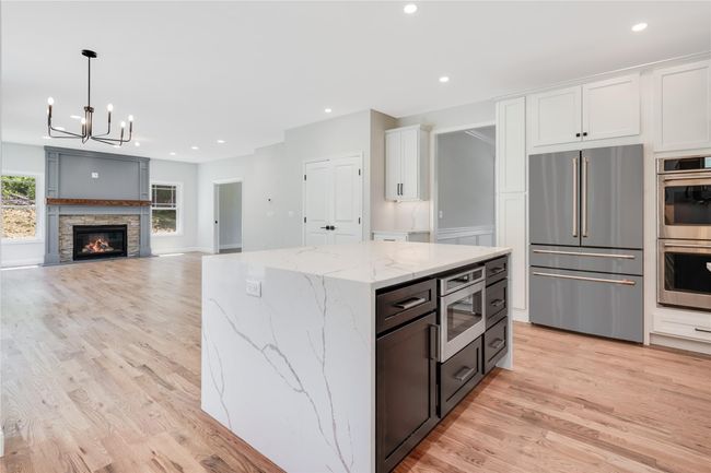 Kitchen with light countertops, high quality fridge, black microwave, light wood-type flooring, and hanging light fixtures | Image 10