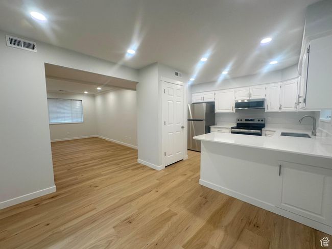Kitchen with stainless steel appliances, light countertops, light wood-style floors, a peninsula, and white cabinets | Image 9