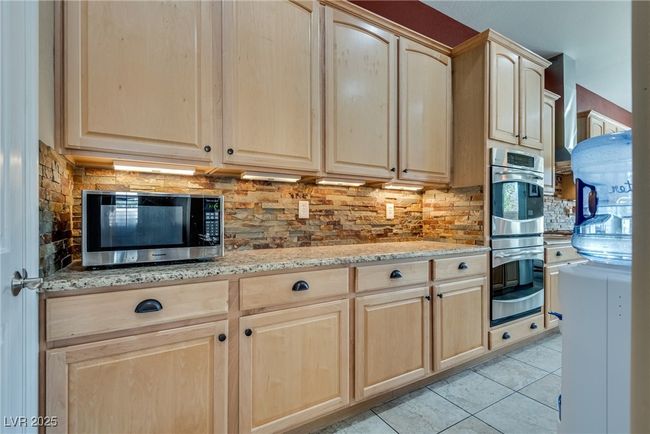 Kitchen with tasteful backsplash, light brown cabinetry, light tile patterned flooring, light stone counters, and appliances with stainless steel finishes | Image 21